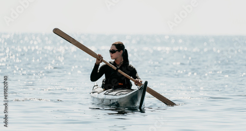 Woman sea kayak. Happy smiling woman in kayak on ocean, paddling with wooden oar. Calm sea water and horizon in background. Active lifestyle at sea. Summer vacation.