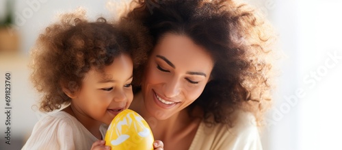 Brazilian child happily embraces woman at home with Easter egg.