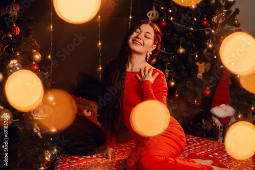 Beautiful young woman in red dress in New Year's atmosphere with garlands in the background. Holiday atmosphere