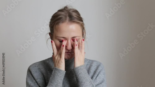 A young girl in a cozy gray sweater rubs her eyes from fatigue. The girl rubs her eyes. photo