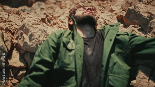 Man with beard falls backwards painfully onto rugged desert rocks, top view