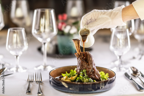 The chef or waiter finishes the meal right on the restaurant table, pouring the sauce over the leg of lamb confit photo