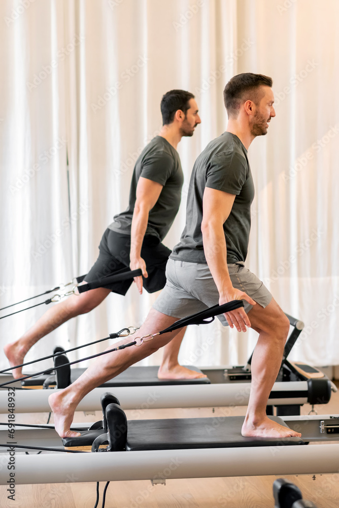 Fit men doing pilates exercises on reformer beds at gym Fit men doing pilates exercises on reformer beds at gym