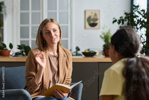 Sosial worker with notebook talking to child during their meeting at home photo