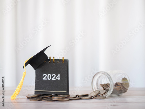 2024 desk calendar with graduation hat on stack of coins. The concept of saving money for education, student loan, scholarship, tuition fees in Year 2024