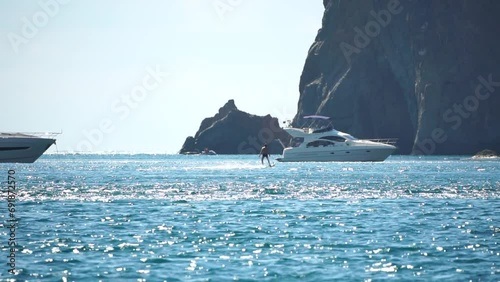 A motorized surfboard with a rider moving on a calm sea. The silhouette of a man on a water scooter glides through the water. Sports and sea activities on a beach holiday. Slow motion. photo