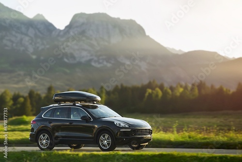 Black luxury SUV with Luggage box mounted on the roof. Adventure on the road. Roof box for car extra capacity in action