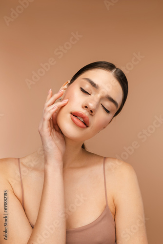 Portrait of tender young woman with perfect face posing at camera. Isolated on beige background. Skin care, beauty procedure, morning routine concept