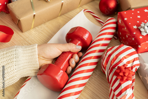 Fotografie Woman wrapping a red dumbbell in paper, packing Christmas gifts