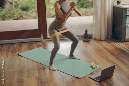 Close up of woman in activewear doing squats with fitness elastic band on mat at home photo