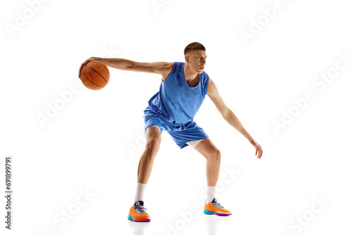 Young man in blue uniform, basketball player in motion during game, dribbling ball isolated over white background. Concept of professional sport, competition, match, championship, health, action. Ad