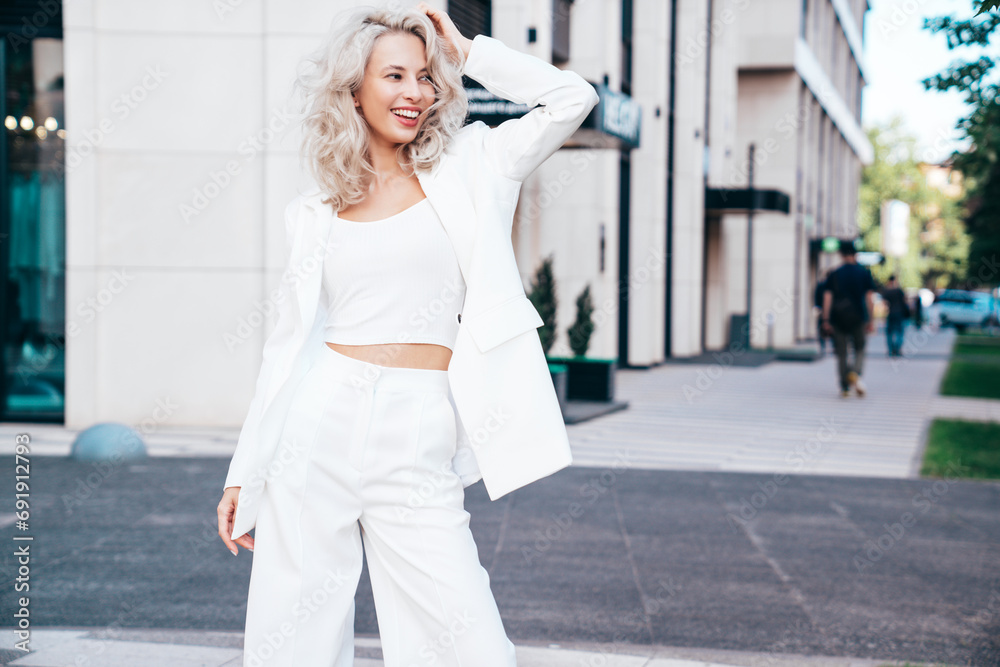Young beautiful blond woman wearing nice trendy white suit jacket. Smiling model posing in the street at sunny day. Fashionable female outdoors. Cheerful and happy Young beautiful blond woman wearing nice trendy white suit jacket. Smiling model posing in the street at sunny day. Fashionable female outdoors. Cheerful and happy