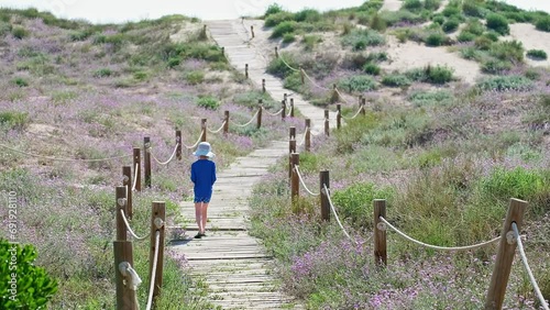  Child walks to the beach front by the wooden path during summer vacation.