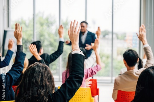 Business professionals come together for a corporate event featuring a conference and convention. Raised hands demonstrate active involvement in a meeting training seminar and discussions. photo