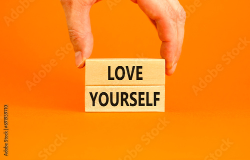 Love yourself symbol. Concept words Love yourself on beautiful wooden blocks. Beautiful orange table orange background. Businessman hand. Psychology love yourself concept. Copy space. photo