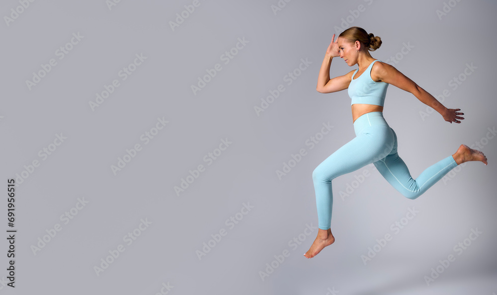 Studio Shot Of Woman Wearing Gym Fitness Clothing In Mid-Air Exercising On Grey Background Studio Shot Of Woman Wearing Gym Fitness Clothing In Mid-Air Exercising On Grey Background