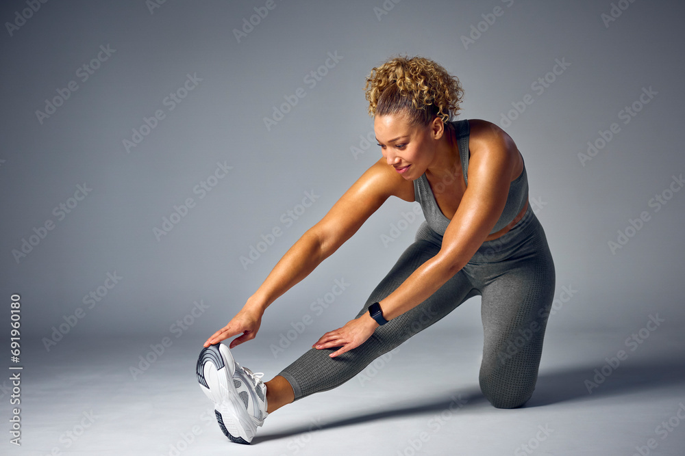 Obraz premium Studio Shot Of Woman In Gym Fitness Clothing Wearing Fitness Tracker Stretching On Grey Background