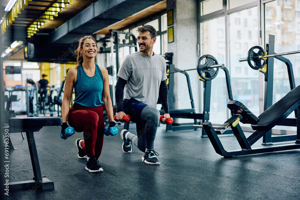Happy athletic couple exercising with hand weights in lunge position in gym. - obrazy, fototapety, plakaty 