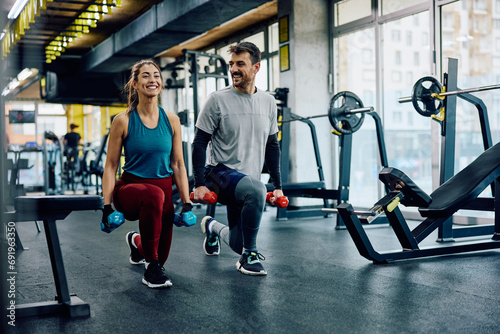 Happy athletic couple exercising with hand weights in lunge position in gym. photo