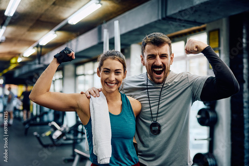 Happy athletic woman and her fitness instructor flexing muscles in gym while looking at camera. photo