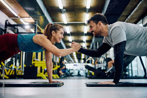 Happy athletic couple cooperating while exercising in plank pose in gym. photo