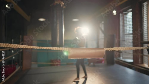 Afro american woman boxer with curly hair boxing in gym on boxing ring and resting on rope. Young girl boxing training punches and hits on punching bag. Professional sport, workout, training concept. photo