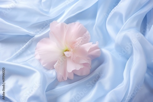  a pink flower sitting on top of a light blue sheet of a sheet of light blue fabric with a light pink flower in the center of the center of the image.