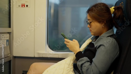Young asian woman passenger using smartphone sitting in chair on train near window. Woman traveler holding phone while traveling by suburban train. Japan transportation