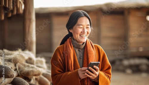 Traditional Chinese woman in village,farm landscape watching on her mobile phone and laughing. Asian elderly woman using smartphone,social media or texting in China