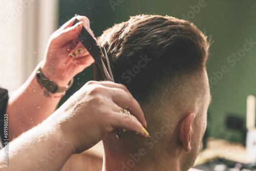 Girl hairdresser doing hairstyle and styling with scissors and comb to a young man