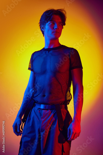 Handsome muscular young man in stylish extraordinary clothes posing over colorful background in neon light. Concept of youth culture, fashion and male beauty, emotions, inspiration, trends