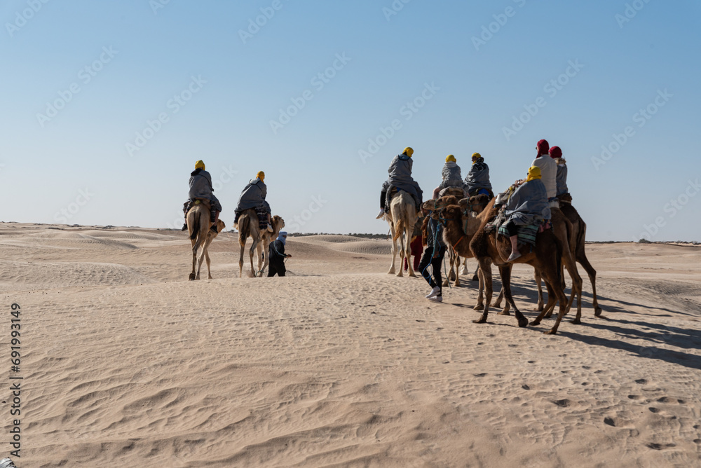 Sahara, Tunisia - April 3, 2023: Caravan with camels in the desert. Tourist attractions in Tunisia. Trip to the desert on camels.