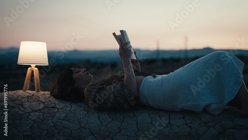 Girl reads a book on a rock with abat jour in the evening photo