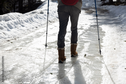 Woman Hiker Walking Carefully over part of Frozen Icy Road in Winter in Snowshoes and with help of Hiking Poles