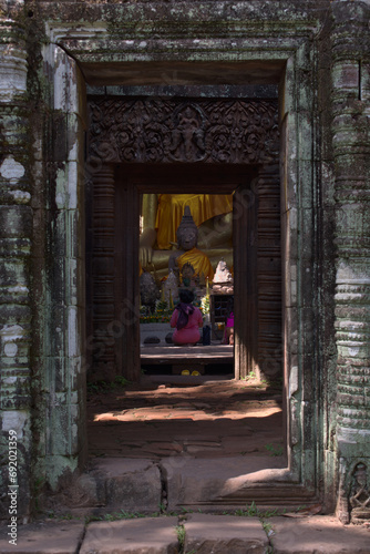 Woman praying inside a Buddhist temple with the door as a frame and Buddha in the center © Pedro