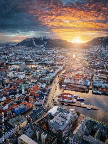 Aerial winter sunrise view of the cityscape of Bergen, Norway, with golden sunlight hitting the snow capped mountains