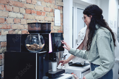 Canvas Print Young woman preparing fresh aromatic coffee with modern machine while standing in the office lobby