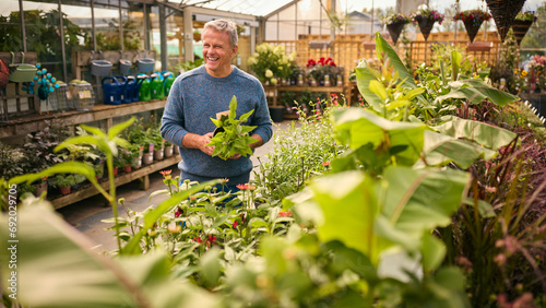 Mature Man Inside Greenhouse In Garden Centre Choosing And Buying Plants