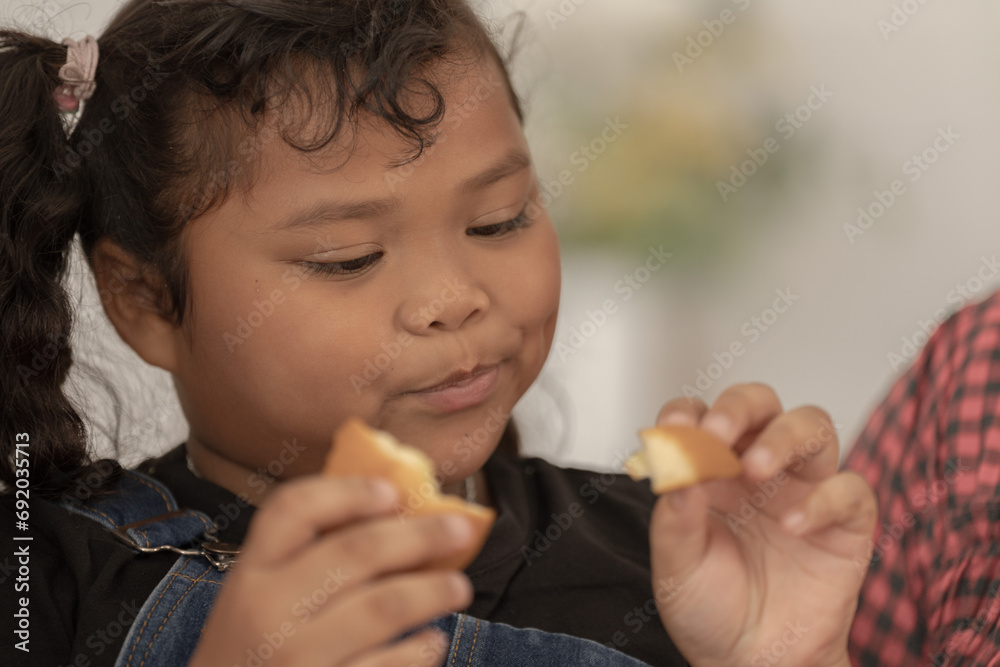 close up face of a Cute Asian girl eating a snack with family. Pretty Black Child Eating Snack At Home. Preschool Kid Having A Bite With Fresh Baked Biscuits. close up face of a Cute Asian girl eating a snack with family. Pretty Black Child Eating Snack At Home. Preschool Kid Having A Bite With Fresh Baked Biscuits.