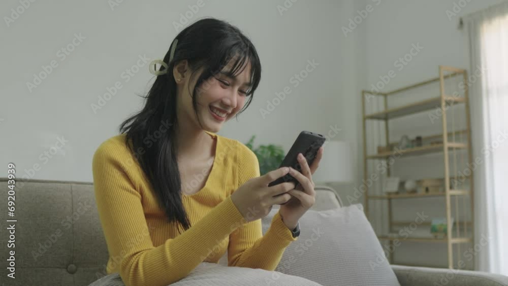 Happy young asian woman relax on comfortable couch at home texting messaging on smartphone, smiling girl use cellphone, chatting online message, shopping online from home