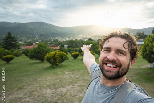 Young hiker taking a selfie portrait at the top of a viewpoint. Happy guy smiling at the camera. Hiking, sport, travel and technology concept. Bright filter. photo