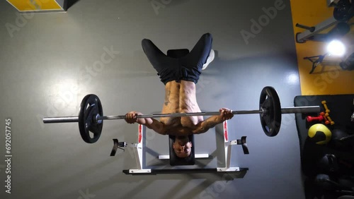 Muscular african man doing bench press workout with a barbell at sport club. Young afro american sportsman doing weightlifting exercises at modern gym. Healthy and active lifestyle concept. Top view photo
