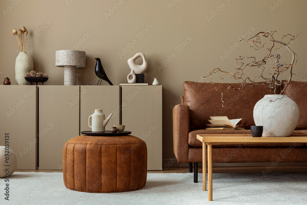 Warm and cozy living room interior with brown sofa, wooden coffee table, round pouf, vase with branch, beige sideboard, pitcher, cup, books and personal accessories. Home decor. Template. - obrazy, fototapety, plakaty 