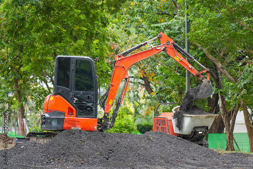 Orange mini excavator in operation digs and loads in the back of a mini stretcher bulldozer fertile soil in the park. photo