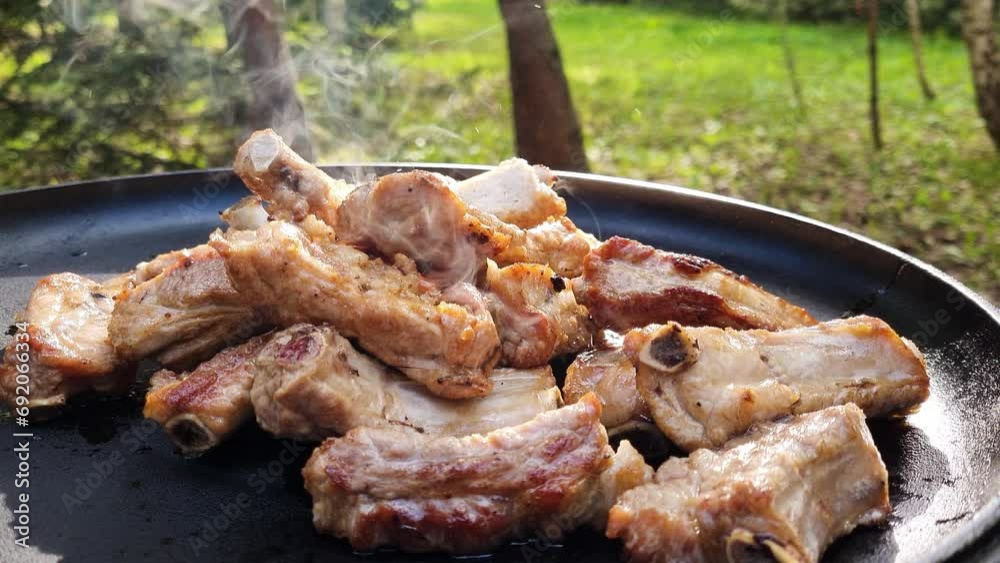 Cooking outdoors with cast iron pan. Frying pork ribs. 4k video footage UHD 3840x2160