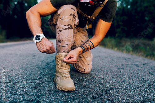 Crop anonymous Mature male commando tying shoelace while kneeling on road photo