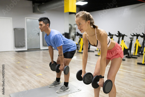 Young man and woman doing dumbbell exercises at the gym