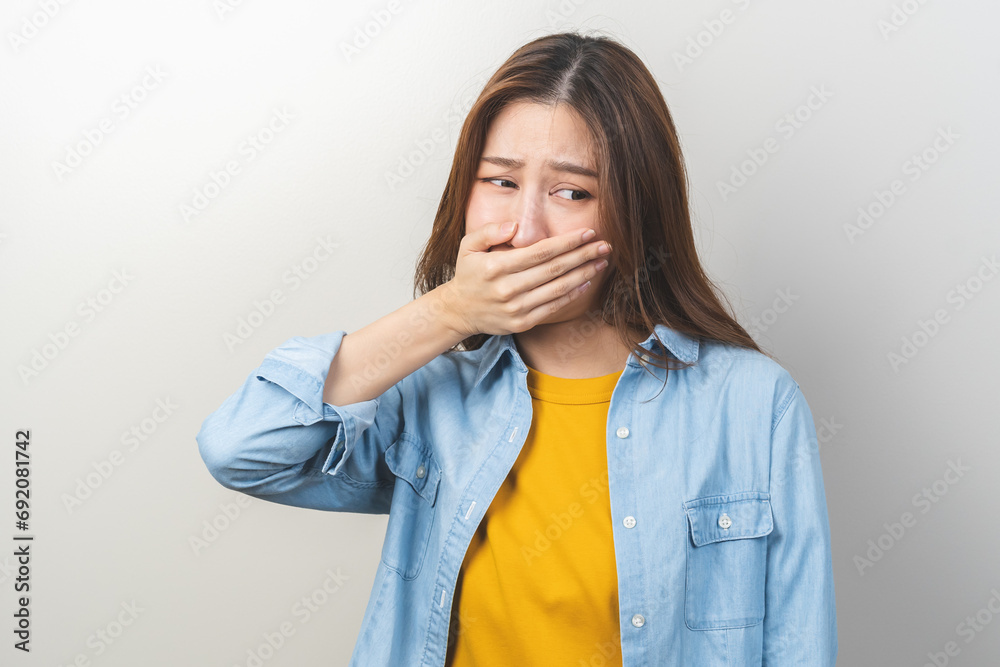 Portrait of pretty brunette hair, disgust smell bad breath strong asian young woman, girl covering, close her mouth with hand, expression face disgusting, dislike odor. Isolated on white background.