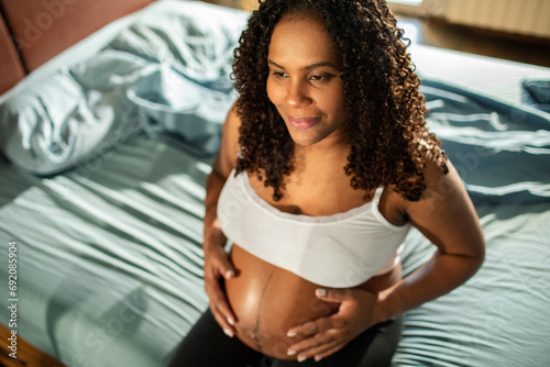 Young pregnant latin woman holding her belly in the bedroom photo