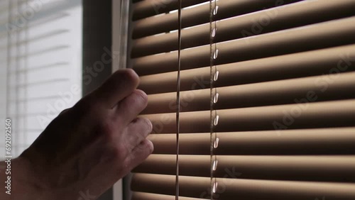 The male hand rotates the handle to close the horizontal blinds, blocking the light from the street. Window blinds open and close.